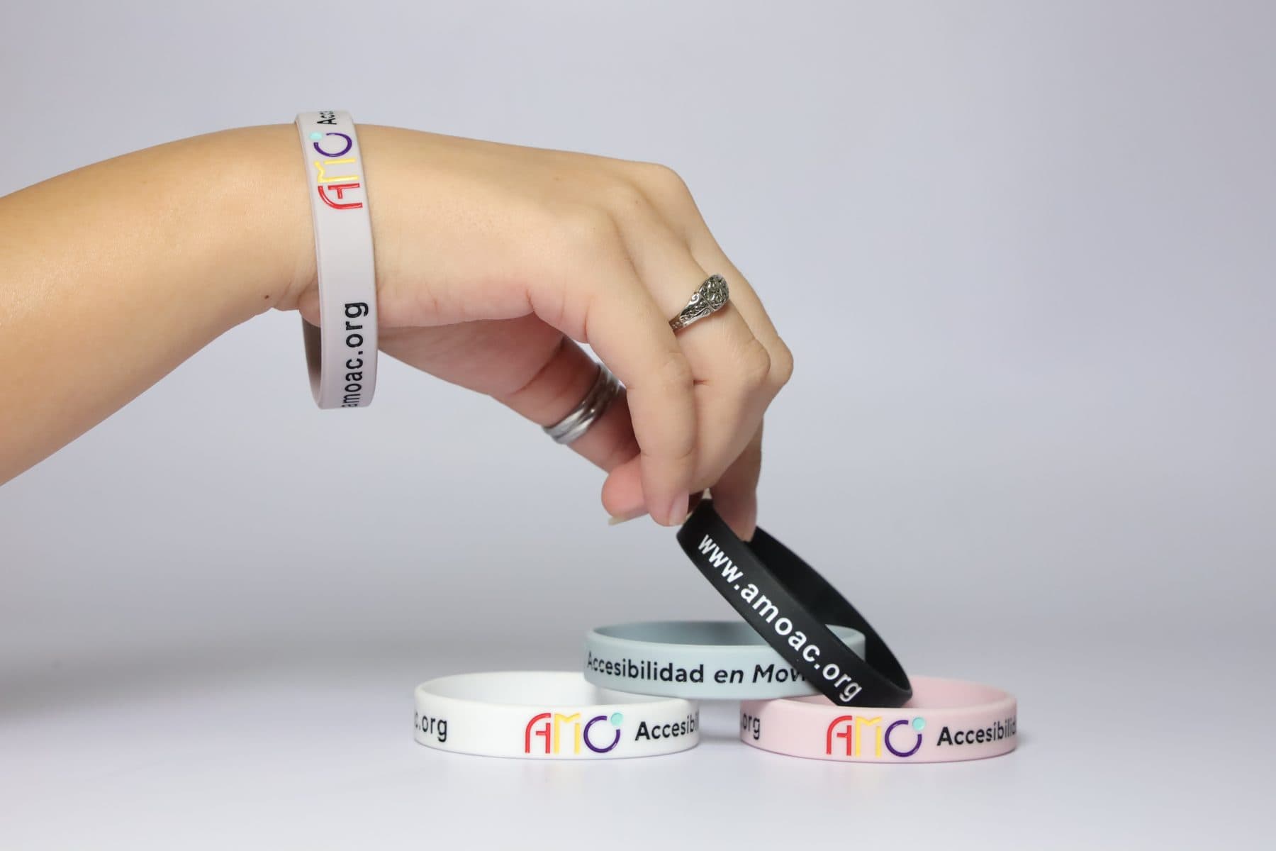 Una mano con la pulsera blanca toma una pulsera negra que dice www.amoac.org