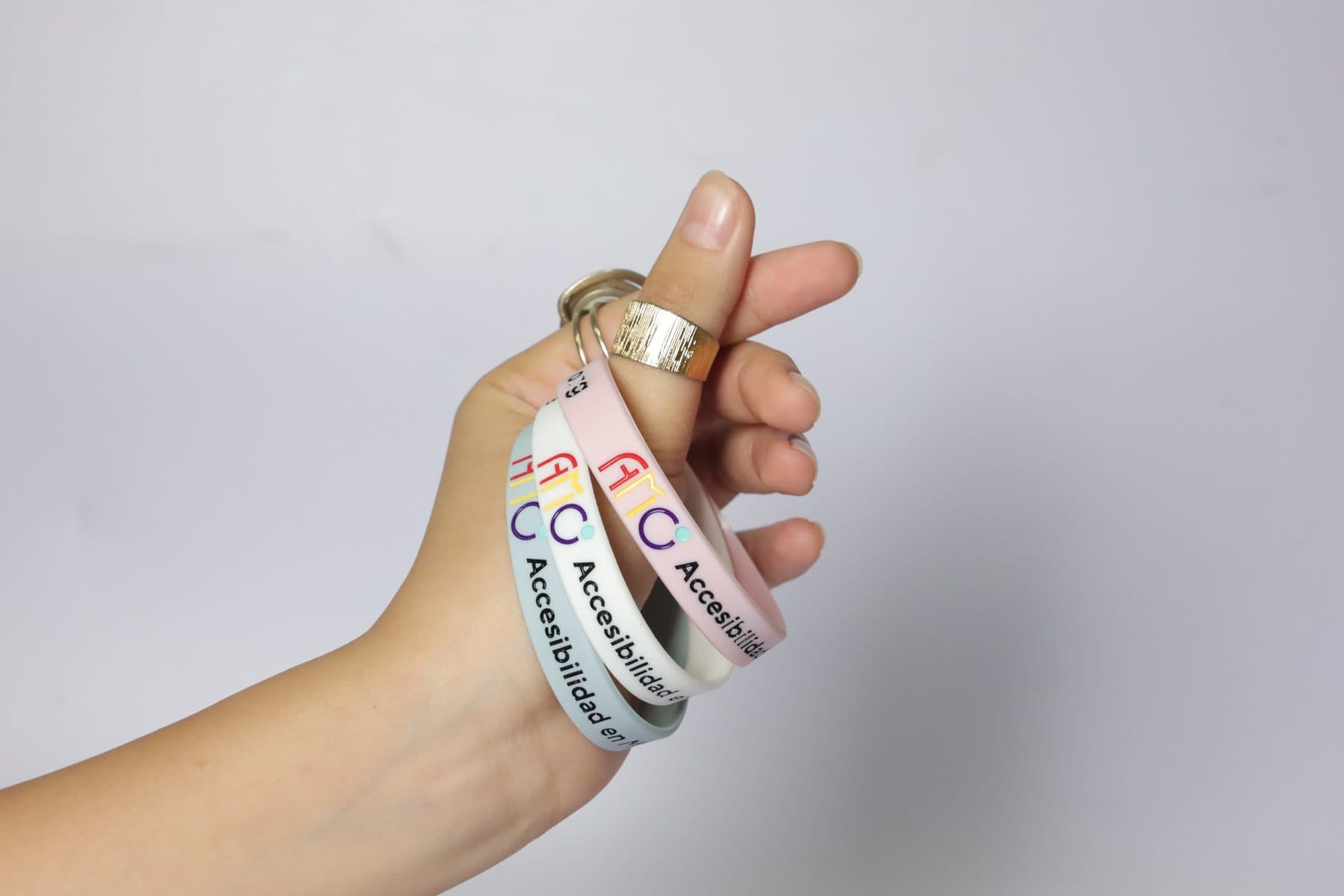 Una mano sostiene pulseras rosa, blanca y lila entre los dedos