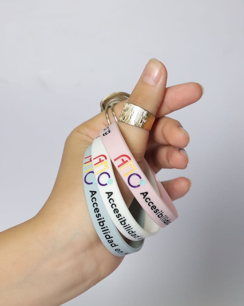 Una mano sostiene pulseras rosa, blanca y lila entre los dedos