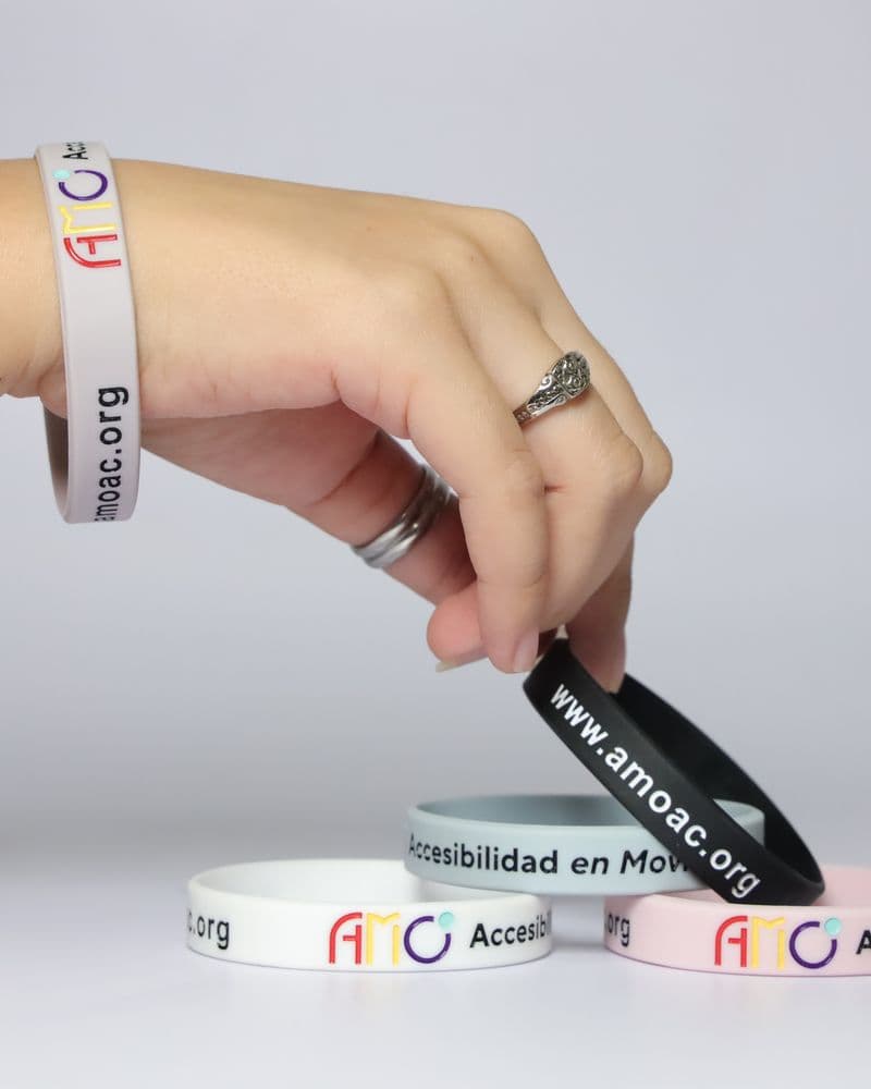 Una mano deja caer una pulsera negra sobre otras pulseras de colores