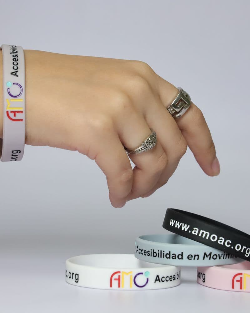 Una mano con pulsera blanca toma una pulsera negra que dice www.amoac.org